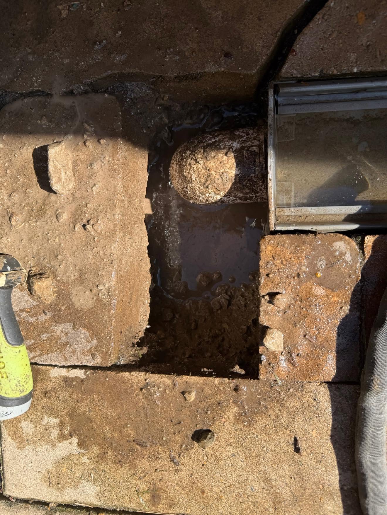 Patio trench drain outlet exposed for cleaning in Linden Estates, Omaha — PVC elbow set in mortar bed under flagstone pavers